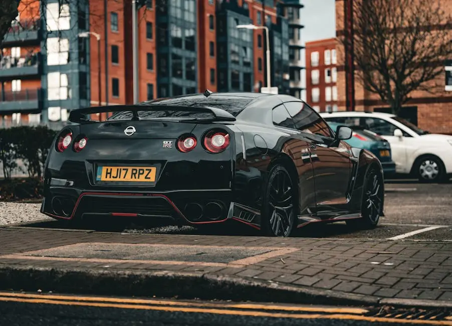 A black sports car parked on a city street, with modern apartments in the background. This sleek vehicle, perhaps transported by leading auto transport companies, boasts a distinctive rear spoiler and a visible license plate. It's overcast, accentuating the car's design against the urban setting.