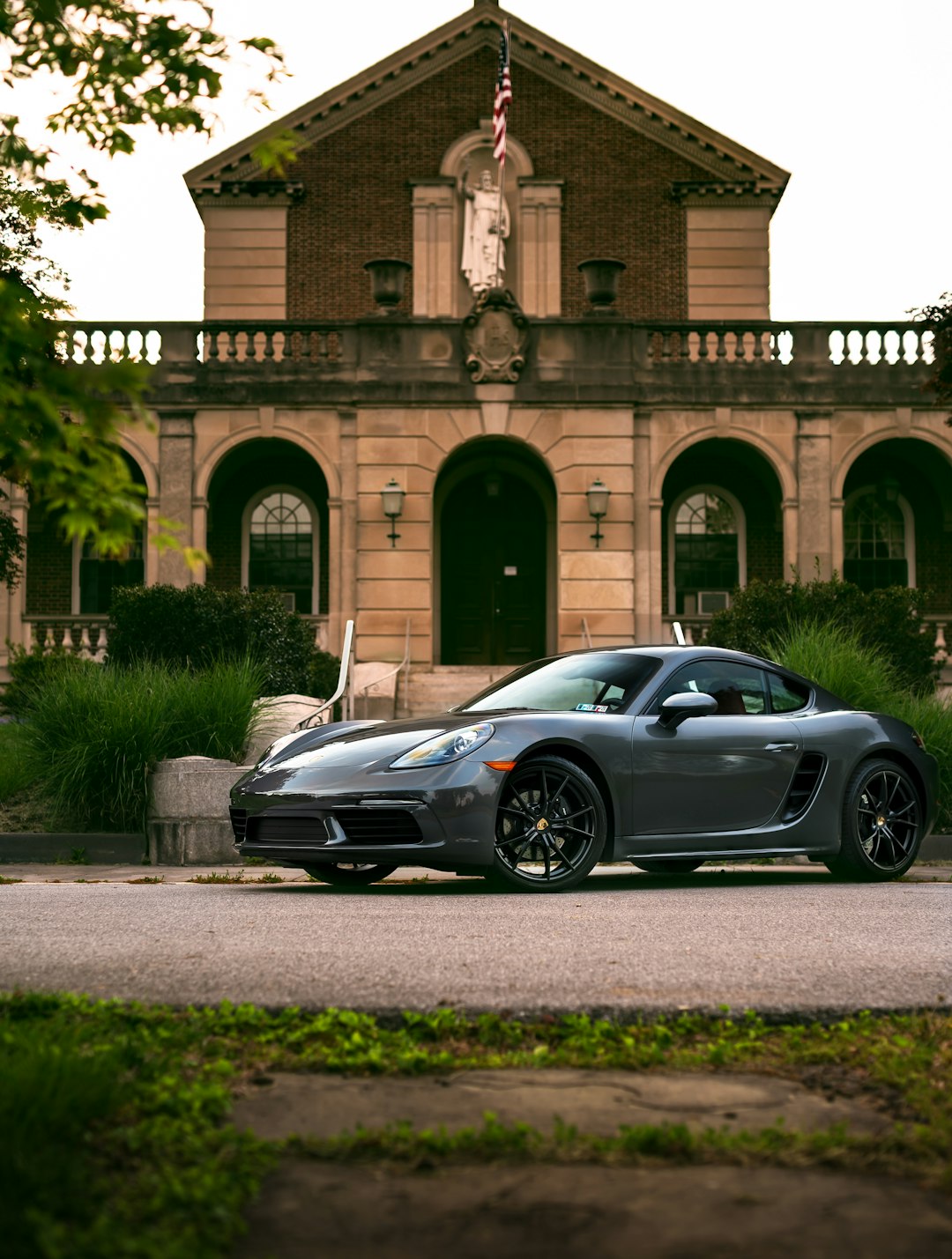 A sleek gray sports car, like those often seen in an essential guide to Chicago auto transport services, is parked in front of a historic brick building with arches and a statue. The scene is framed by greenery, and the building façade features classical architectural elements.